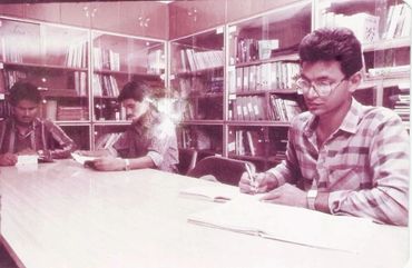 Three young men studying in a library with bookshelves in the background.