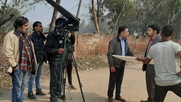 A film crew shoots a scene outdoors with two actors and camera equipment.