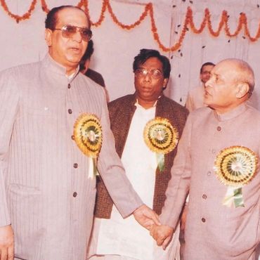 Two men holding hands wearing badges at an event, with a third man in the background.