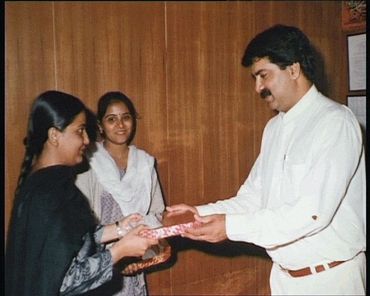 A man in white handing a gift to a woman, with another woman observing.