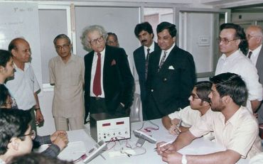 A group of men in formal and casual attire gathered around a table with electronic equipment.