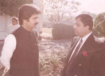 Two men engaged in conversation outdoors, dressed formally.