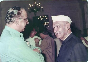 Two elderly men engaged in a conversation at a social event indoors.