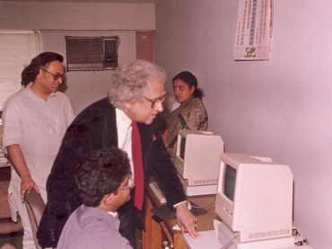 A group of people interacting with vintage Macintosh computers in an office.