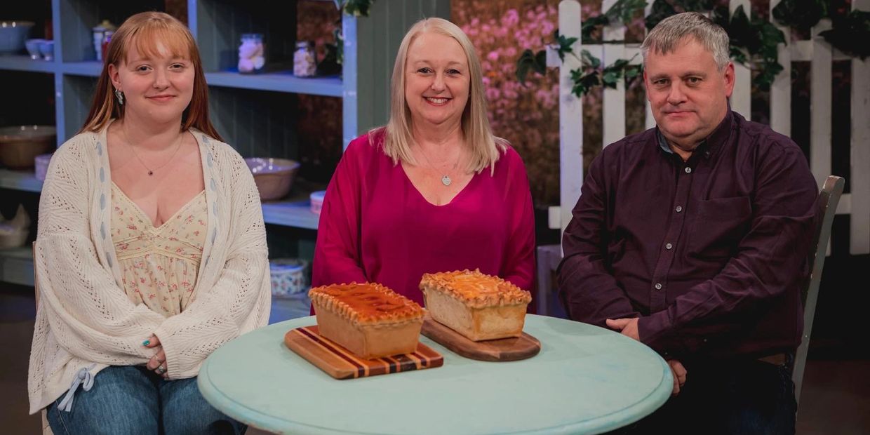 Three people sat at a table on the set of 'Bake Off: An Extra Slice'. L-R: Elizabeth, Denise and Bru