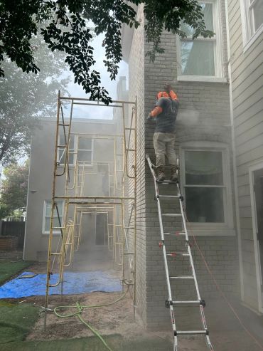Heritage mason raking out old mortar from a brick wall on a ladder, Richmond VA