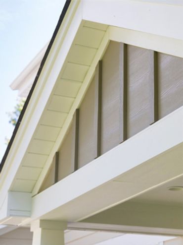 Close-up of a home's roof gable with white trim and gray siding panels.