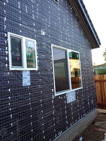 House wall under construction with black mesh and windows installed.