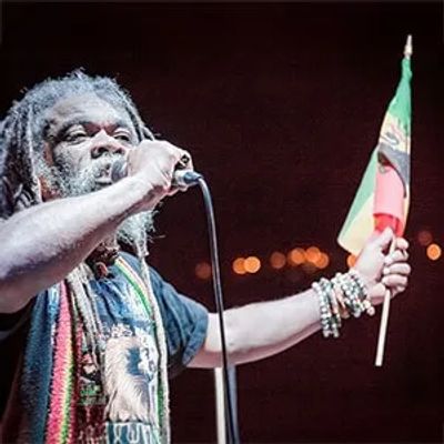 Man singing into microphone holding a colorful flag.