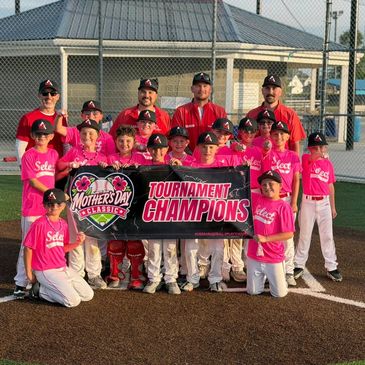 Youth baseball team in pink shirts holding a 'Tournament Champions' banner.