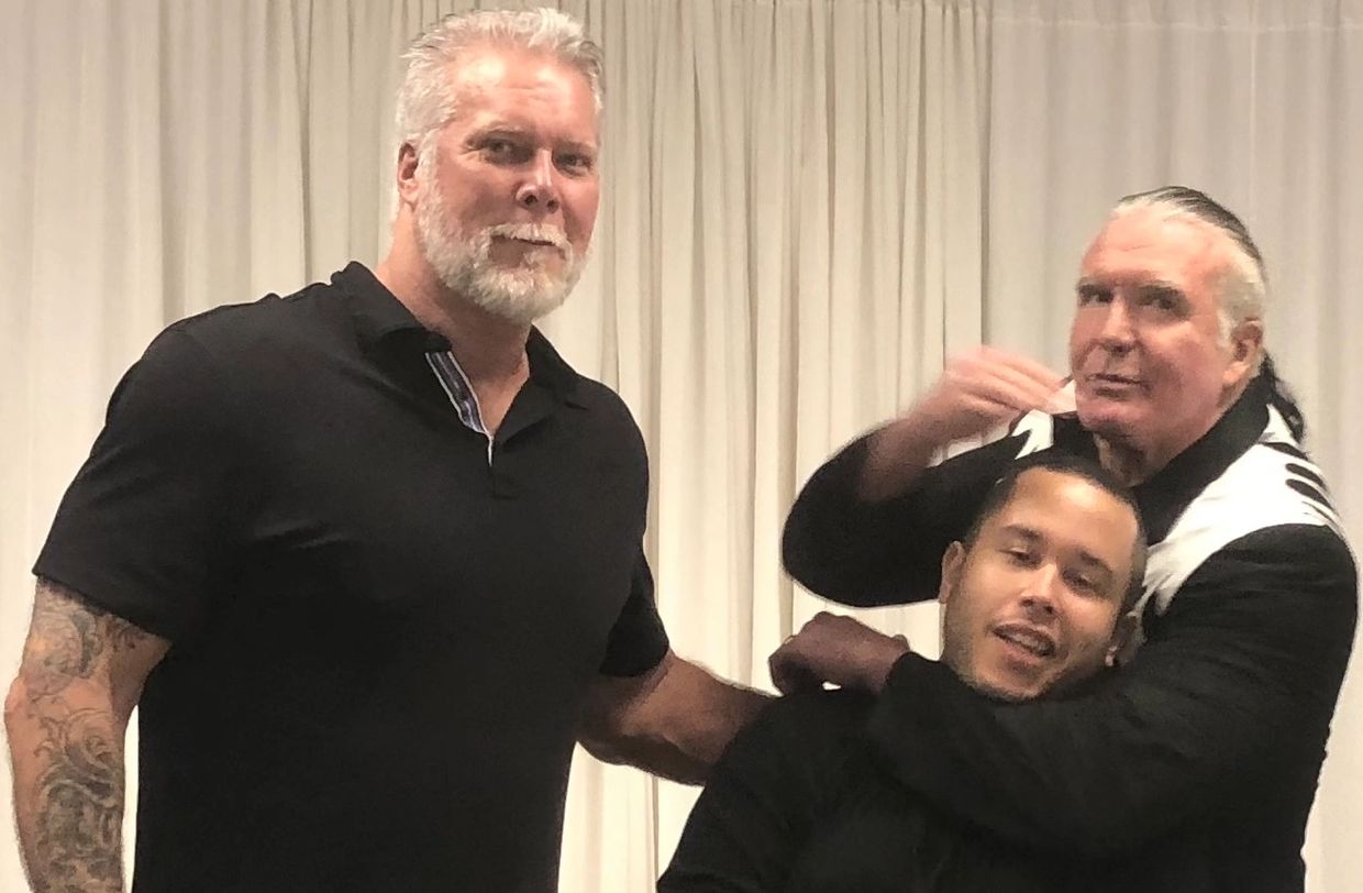 Three men posing playfully in front of a curtain, one giving a mock chokehold.