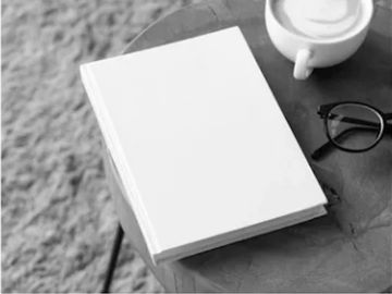 Blank book on a table beside coffee and glasses.