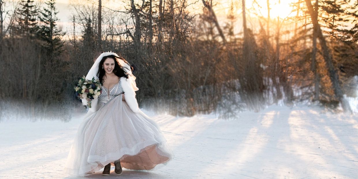 Bride joyfully running in snow with bouquet at sunset.