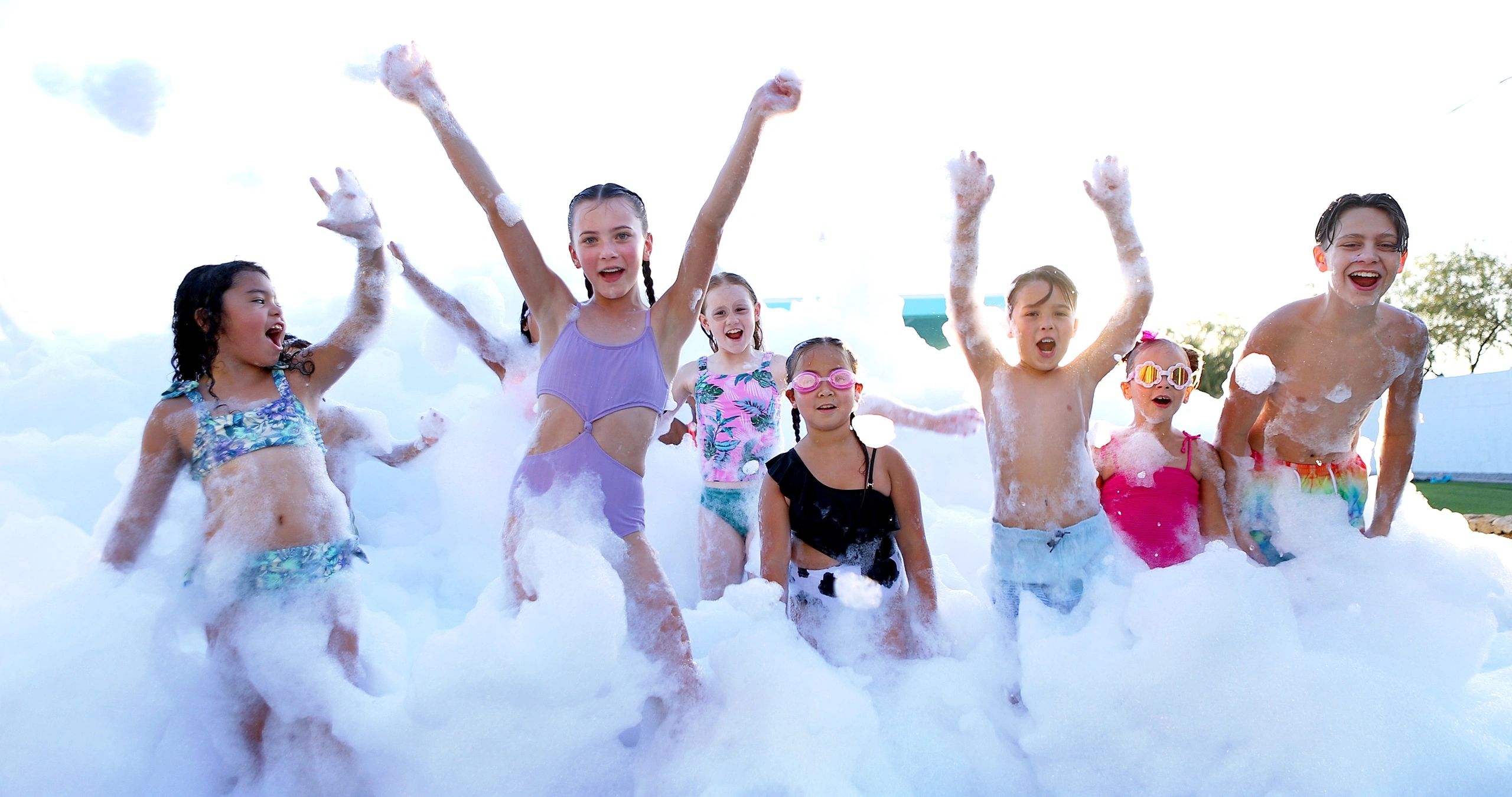 Children joyfully playing in a large foam party outdoors.