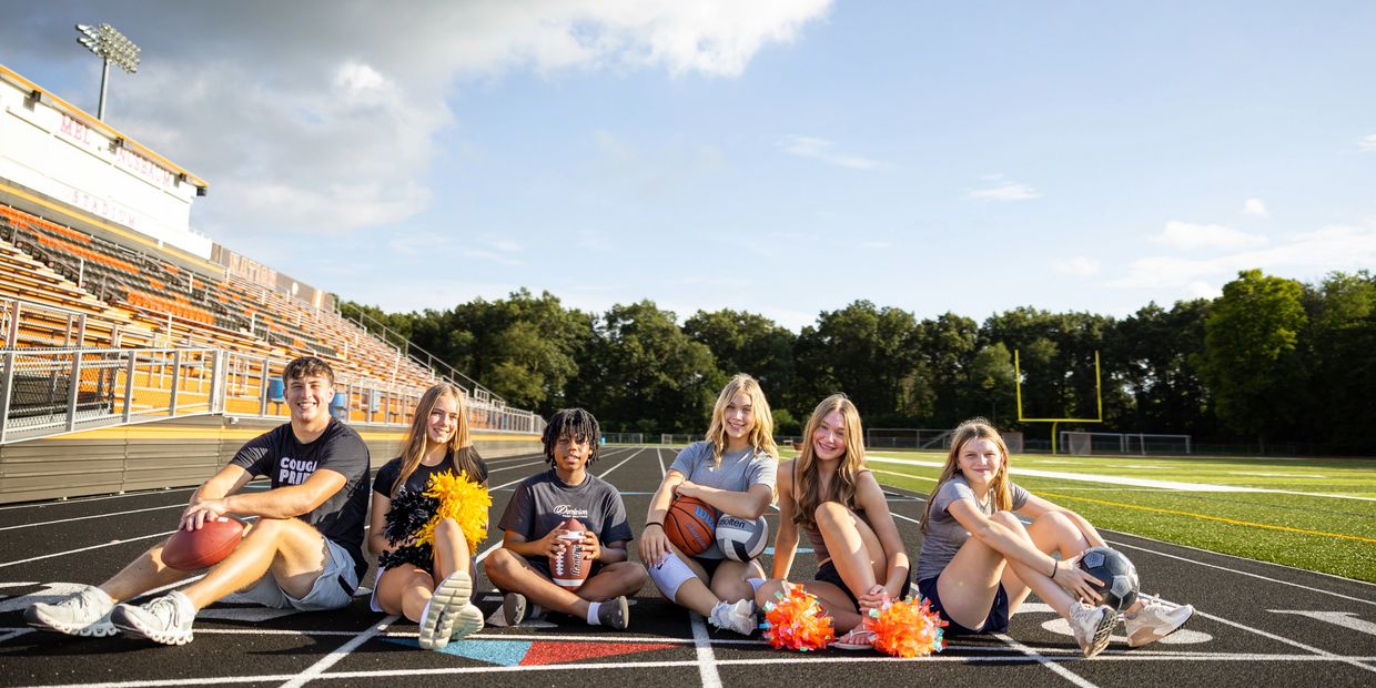 Group of young athletes sitting on a track with sports equipment.