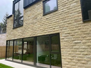 Modern house exterior with large glass windows and beige brick walls.