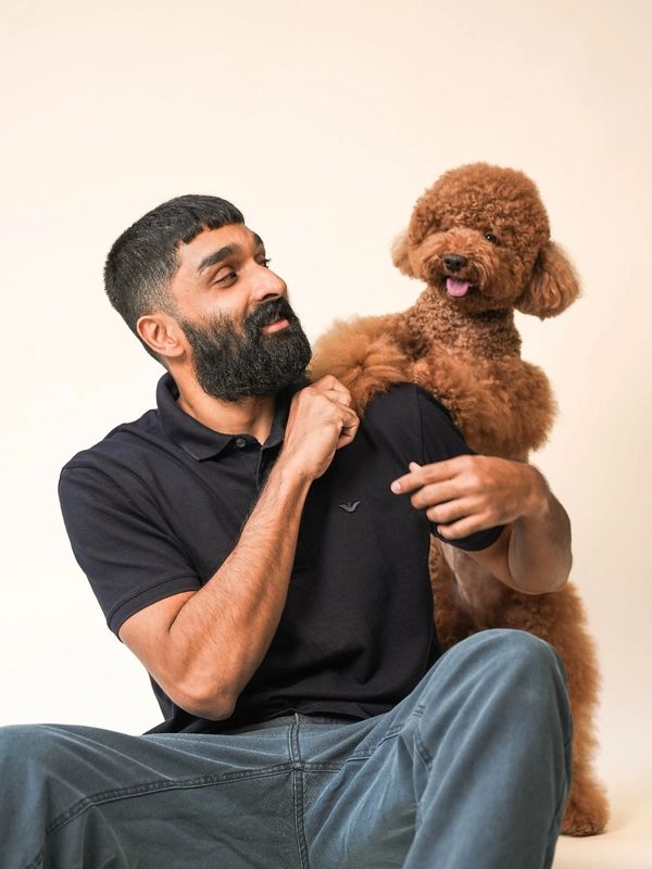 Man with beard playing with a curly-haired brown dog on his shoulder.