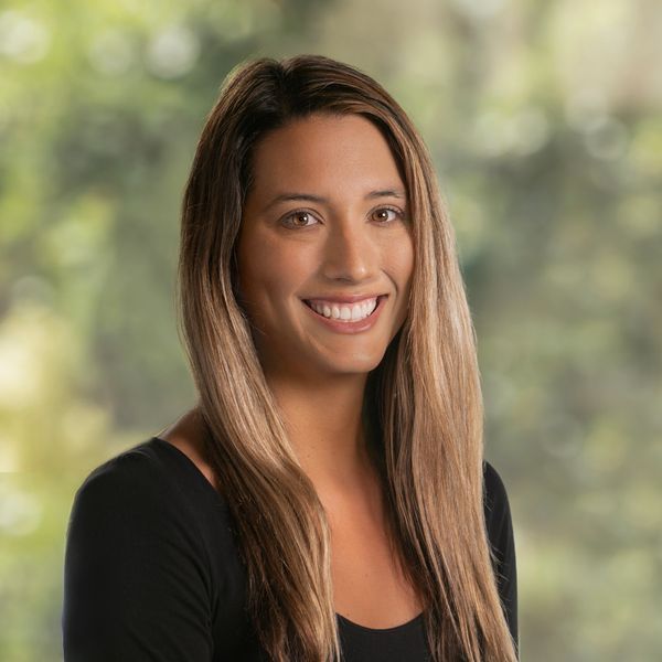 Smiling woman with long hair in a black top against a blurred natural background.