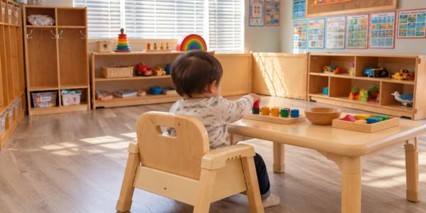 Child playing with colorful toys at a wooden table in a bright classroom.