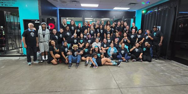Large group of people posing indoors, many wearing matching black shirts.