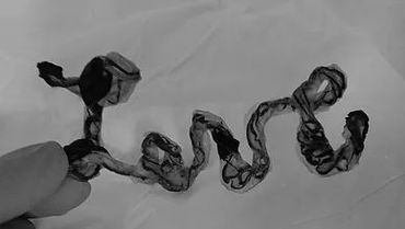 Hand holding a twisted, black, ribbon-like object on white paper.