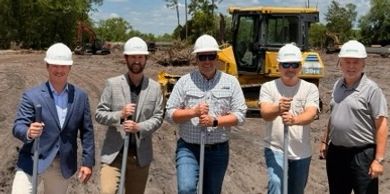 Five men in hard hats with golden shovels at a groundbreaking ceremony on a sunny day.