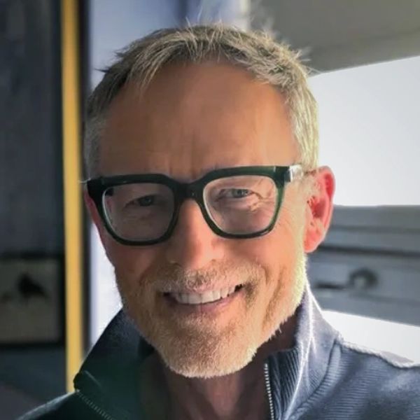 Smiling middle-aged man with glasses and gray hair indoors.