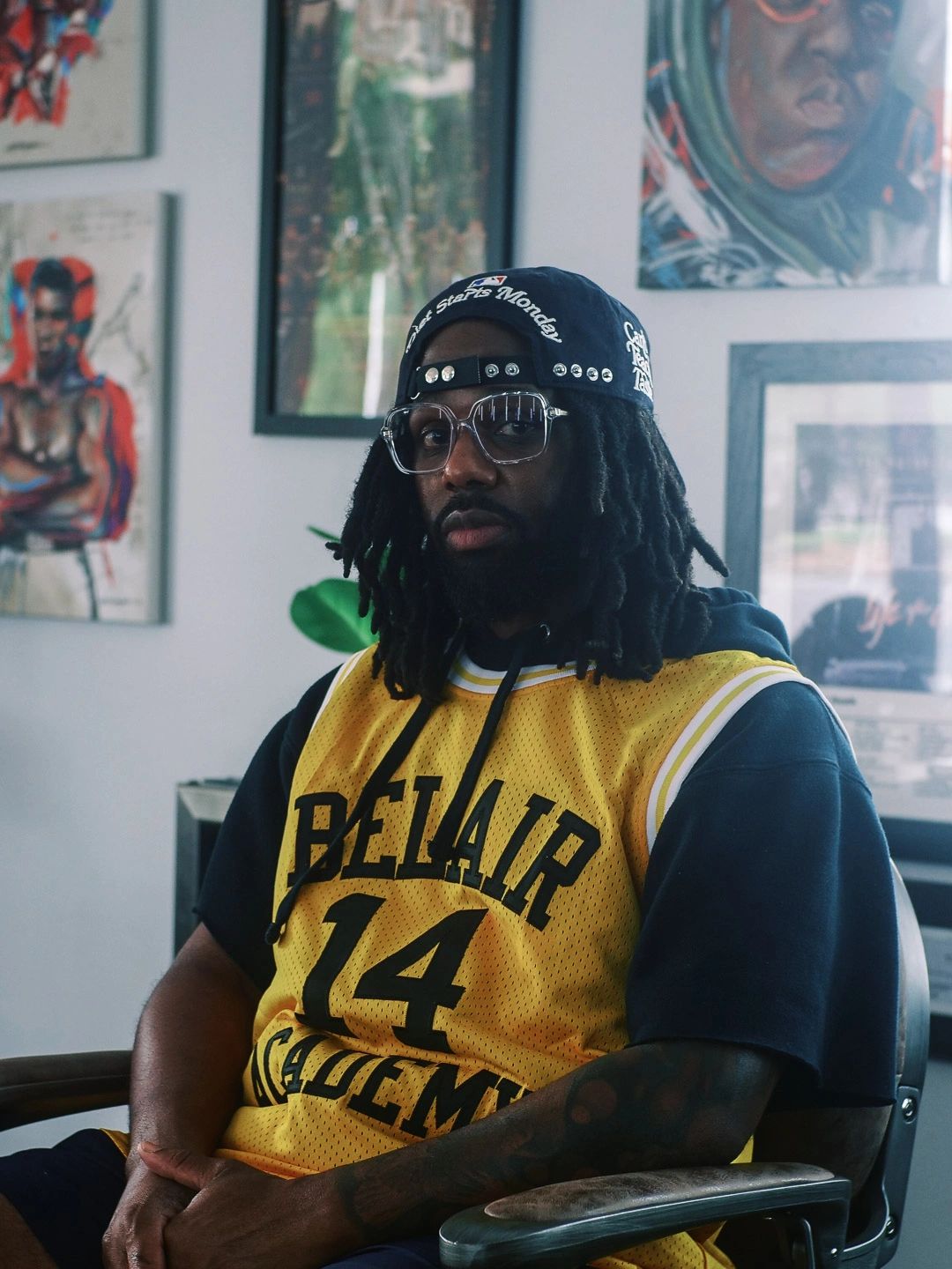 Man in a yellow Bel-Air Academy jersey and cap sitting indoors.