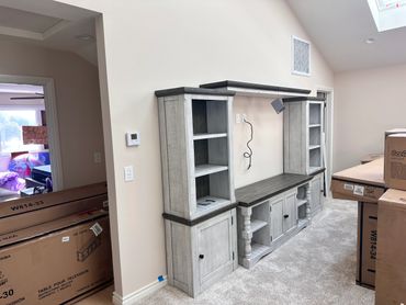 Newly assembled gray wooden entertainment center in a bright room with unpacked boxes.