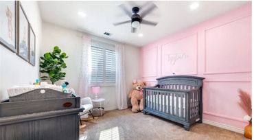 Cozy baby nursery with pink accent wall, gray crib, and large teddy bear.