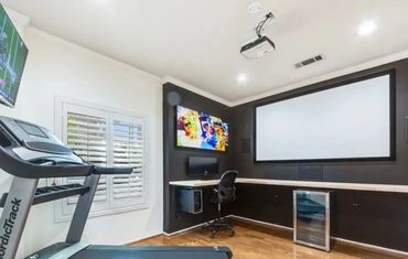 Modern home gym with treadmill and entertainment setup including projector and TV.