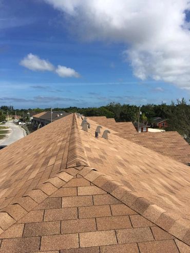 View from the top of a brown shingled rooftop under a blue sky with clouds.