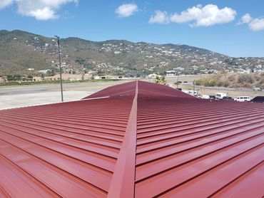 Red metal roof with mountains and airport runway in the background under a blue sky.