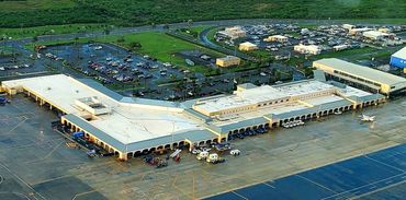 Aerial view of an airport terminal with parked cars and a small airplane on the runway.