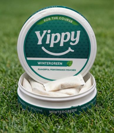 Open container of Yippy wintergreen flavored pouches on grass.