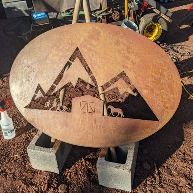 Rusty metal fire pit with mountain and farm cutout design.