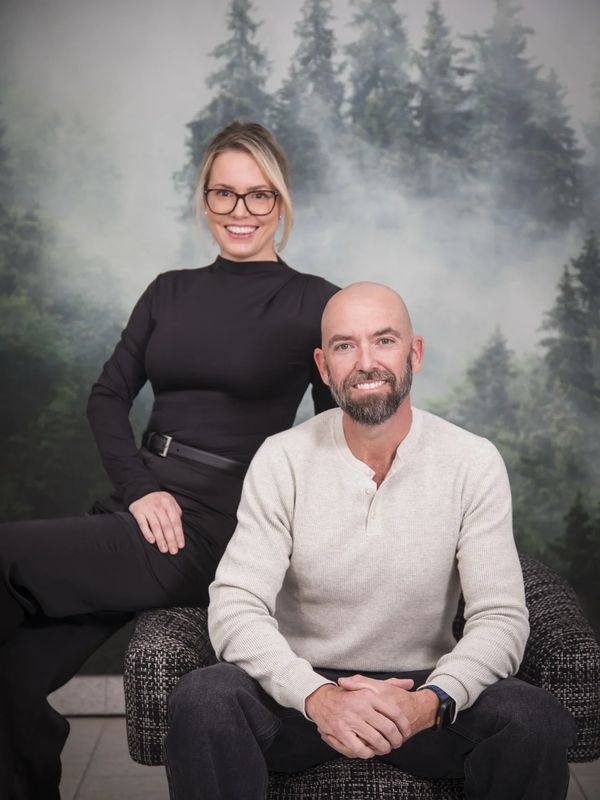 Smiling man and woman pose together indoors with forest wallpaper.