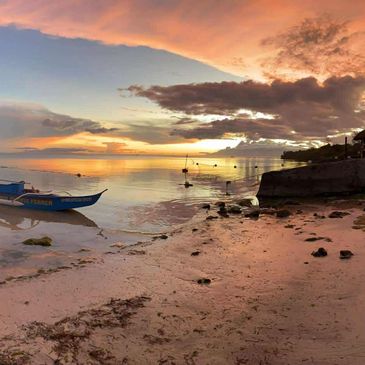 Person capturing a serene sunset by the beach with a boat nearby.