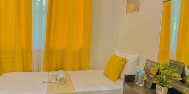Cozy bedroom with yellow curtains, a neatly made bed, and a small plant on the dresser.