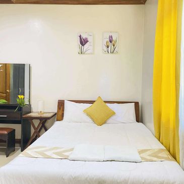 Bright bedroom with yellow curtains, white bedding, and floral wall art.