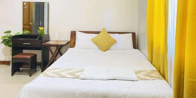 Bright bedroom with yellow curtains, white bedding, and floral wall art.