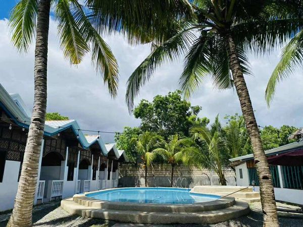 A cozy outdoor pool surrounded by palm trees and cottages under a cloudy sky.