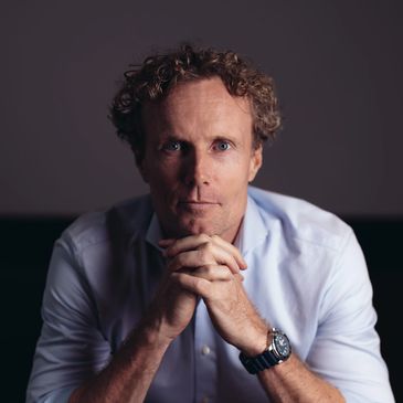 Man with curly hair in white shirt clasping hands.
