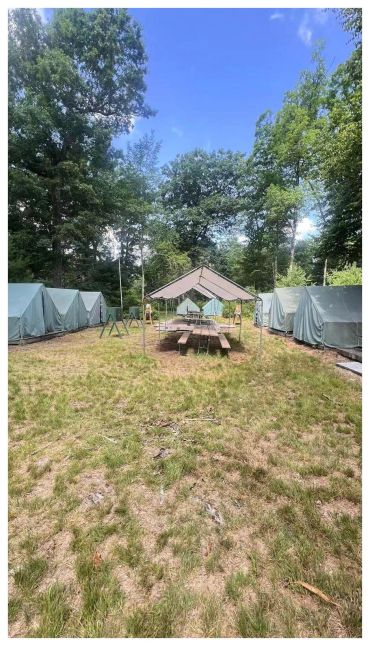 A campsite with tents and a picnic table under a canopy.