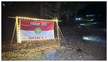 Illuminated Troop 255 Queens NY flag at night outdoors.