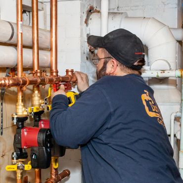 A plumber working on copper pipes with a level tool in a basement.