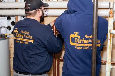 Two plumbers from Durfee Plumbing & Heating working on copper pipes indoors.