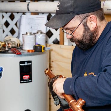 A plumber working on copper pipes with tools near a water heater.