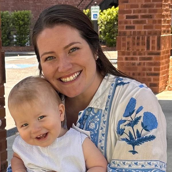 Smiling woman holding a happy baby outdoors near a brick wall.