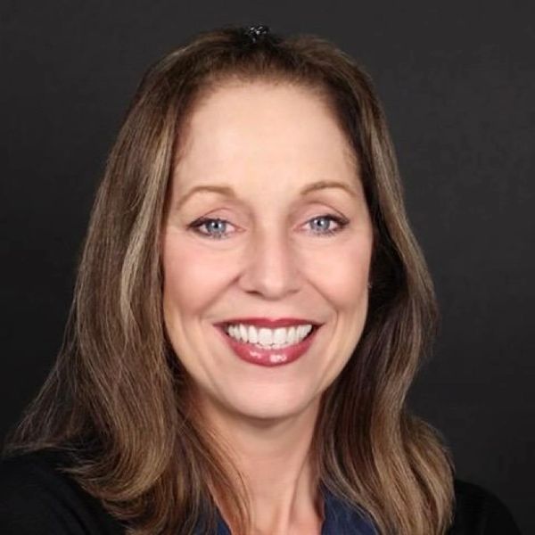 Smiling woman with long brown hair against a black background.
